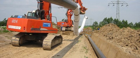 Bagger beim Verlegen von Rohrleitungen an einer Baugrube Bagger beim Verlegen von Rohrleitungen an einer Baugrube