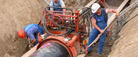 Drei Mitarbeiter arbeiten in einer Baugrube an Rohrleitungen Drei Mitarbeiter arbeiten in einer Baugrube an Rohrleitungen