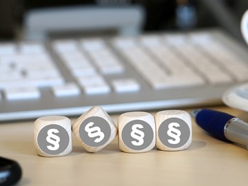 Vier Holzwürfel auf einem Schreibtisch neben einem Kugelschreiber vor einer Tastatur zeigen alle das Paragrafenzeichen Vier Holzwürfel auf einem Schreibtisch neben einem Kugelschreiber vor einer Tastatur zeigen alle das Paragrafenzeichen